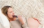 Relaxed future mom eating a chocolate bar lying on the sofa at home