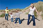 A happy family of mother, father and two sons, walking holding hands and having fun in the sand dunes of a sunny beach