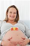 Adorable future mother with mom letters on her belly and smiling at the camera
