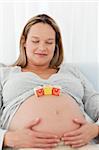 Cute pregnant woman with mom letters on her belly relaxing on a bed