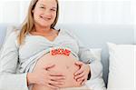 Blond pregnant woman with mom letters on her belly lying on a bed at home