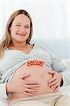 Cheerful young woman with mom letters on her belly and looking at the camera