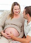 Lovely pregnant woman touching her belly with her husband sitting in the sofa