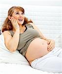 Happy beautiful pregnant woman sitting on sofa at home and holding her belly