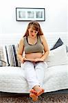 Beautiful pregnant woman sitting on sofa at home and reading book