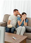 Lovely couple hiding their face from a horror movie sitting in the living-room at home