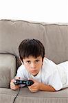 Concentrated boy playing video games lying on the sofa at home