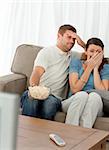 Terrified couple watching a horror movie at home