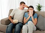 Scared couple eating pop corn while watching a horror movie at home
