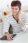 Attractive man talking on phone using his laptop in the kitchen at home