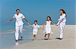 A happy family of mother, father and two children, son and daughter, running holding hands and having fun in the sand of a sunny beach