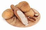 Bread roll selection on a wooden board with wholegrain flour, brown sugar and yeast in scoops, with ears of wheat, over white background..