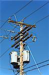 Transformers of an electrical post with powerlines against bright blue sky.