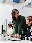 Computer class with caucasian female teacher helping student. Vertical shape, side view, waist up