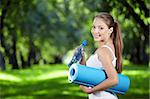 Young girl with a bottle of water and gym mat in the park