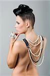 back side portrait of sensual brunette with creative hair style covering her naked shoulder with lots of necklace