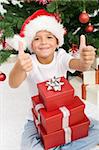 Boy having lots of christmas presents showing thumbs up sign with both hands