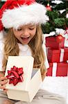 Excited little girl opening christmas present in front of the fir tree - closeup