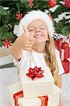 Extremely happy litte girl with thumbs up holding lots of christmas presents