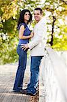 A happy couple in a park on a bridge looking at the camera