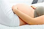 Pregnant woman lying on sofa at home and holding her belly. Close-up.