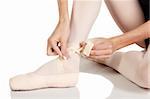 Young caucasian ballerina girl on white background and reflective white floor tying her ballet shoes. Not Isolated