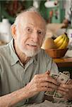 Senior man at home with a few dollars counting his money