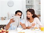 Happy couple reading the newspaper together during breakfast at home