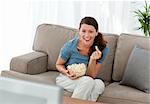 Merry woman eating pop corn while watching a movie on television at home