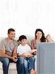 Happy family watching television while eating popcorn together on the sofa