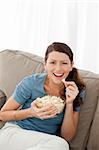 Portrait of a happy woman eating pop corn while watching television at home
