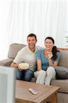 Cute couple eating pop corn while watching television on the sofa at home
