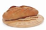 Rye bread loaf on a wooden board with wheat sprigs, over white background.