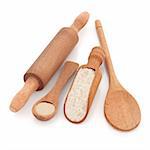 Rustic wooden baking utensils of scoop, spoons and rolling pin with yeast granules and wholegrain flour, over white background.