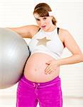 Surprised beautiful pregnant female holding fitness ball and touching her belly at living room