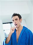 caucasian adult man with bathrobe brushing teeth in bathrooom. Vertical shape, waist up, copy space