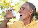 Old man using asthma inhaler out of doors to control allergies. Isolated on white.