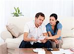 Man showing a bill to his girlfriend sitting on the sofa at home