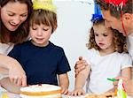 Mom and son cutting a birthday cake together in the kitchen with their family