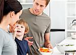 Little boy giving his mother a carrot while preparing lunch in the kitchen