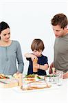 Cute boy putting salt and pepper in his salad in the kitchen with his parents