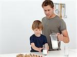 Handsome man giving milk to his son standing in the kitchen