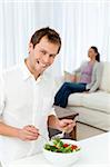 Happy man preparing lunch while his girlfriend relaxing on the sofa