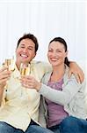 Couple heureux célébrer avec flûte de champagne assis sur le canapé