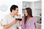 Lovely couple giving a toast with red wine standing in the kitchen