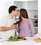 Cute couple kissing while having lunch in the kitchen with red wine
