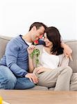Enamored couple sitting together on the sofa playing with a red rose