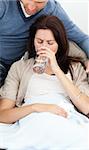 Sick woman drinking water lying on the sofa with her boyfriend
