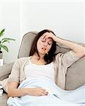 Sick woman taking her temperature with a thermometer on the sofa at home