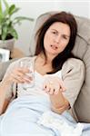 Sick woman taking her medicine on the sofa at home